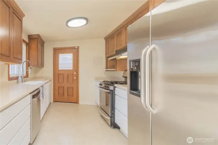 Good size kitchen with two-toned cabinets, stainless appliances, custom Corian counters with bonus cutting board but-outs, with slider to deck