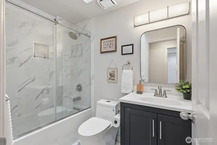 Beautifully remodeled full bathroom with eye-catching patterned tile flooring, updated vanity, mirror, fixtures, and a tiled bath.