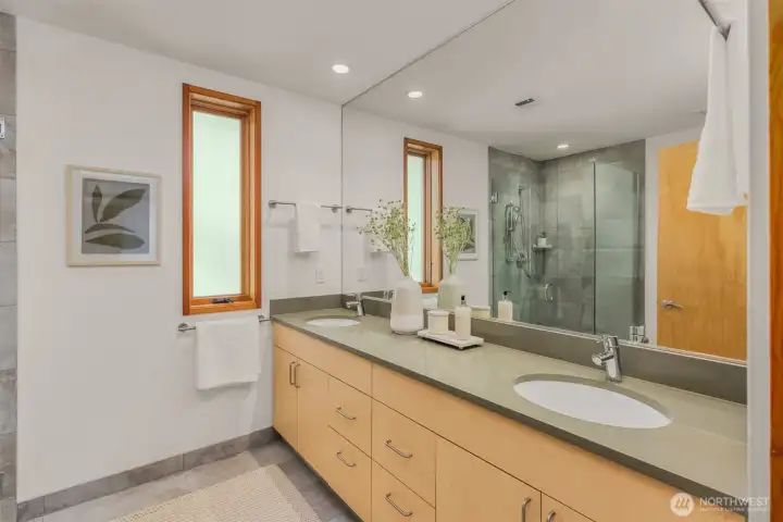 The primary bathroom includes the same soothing palette found throughout the home, here the sage quartz counters house dual under-mount sinks, and natural wood cabinetry provides ample storage space for 2. The primary bathroom includes the same soothing palette found throughout the home, here the sage quartz counters house dual under-mount sinks, and natural wood cabinetry provides ample storage space for 2.
