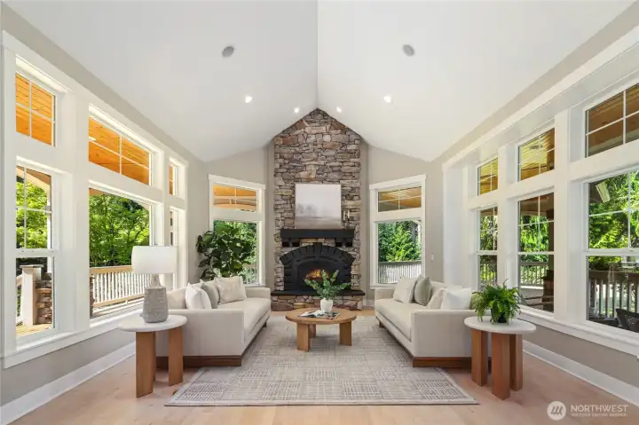 Grand living room wrapped in windows, featuring a striking floor-to-ceiling stone fireplace.