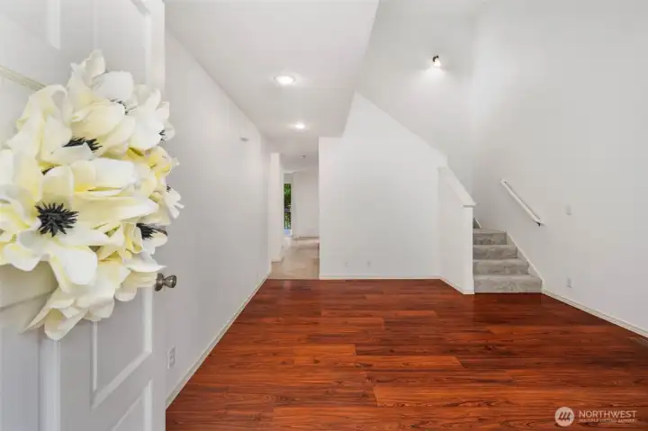 Front Door Entry into Living Room with the stairs on the back right section and hallway on the back left leading to a walk-in closet, 1/2 bathroom, garage access, kitchen, multi-functional living area, back deck.