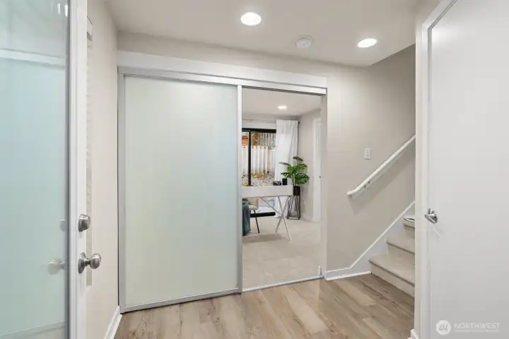 From the moment you enter our townhouse you'll notice the brand-new carpet throughout and LVP flooring in the entryway! This photo is looking into the ground-floor ensuite bedroom and beyond is the slider that leads into the backyard. To the right is the door that opens to the attached one-car garage.