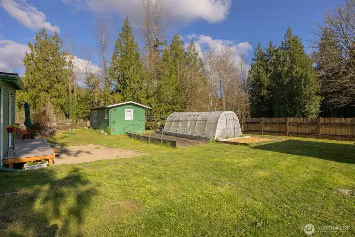 Two hoop-style greenhouses, raised garden beds, and detached outbuilding ideal for shop, studio, or flexible use.