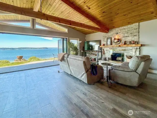 Living room with wood fireplace, vaulted ceilings.  Nano doors can be seen folded back to open the space to the views and outdoors.
