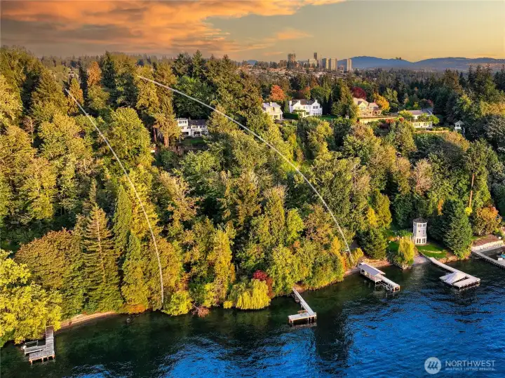 Bathed in the warm light of sunset, this aerial view reveals the rare, preserved beauty of the Evergreen Lakeshore Preserve—a place where the forest meets the water’s edge in quiet harmony. This stretch of Lake Washington shoreline remains one of the Eastside’s last naturally wooded waterfronts, offering a timeless connection to the land, with panoramic city views just beyond the treetops.