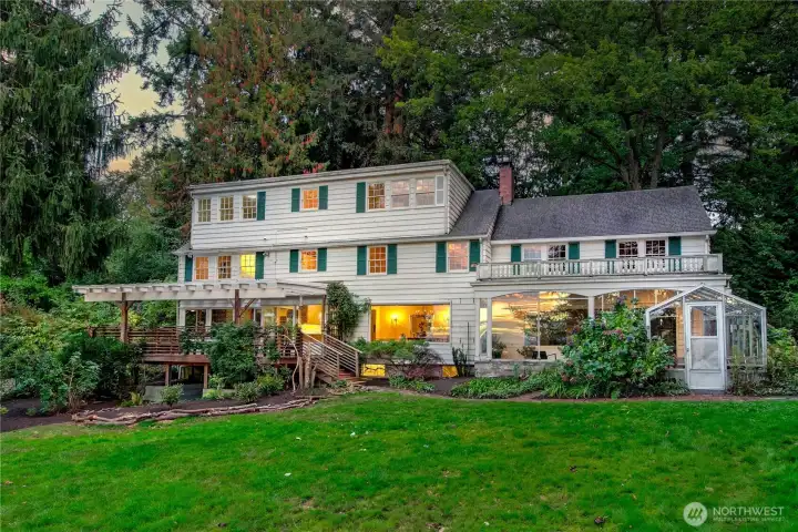 Evening settles softly on the historic residence at Evergreen Lakeshore Preserve, where warm interior light glows through original multi-pane windows, evoking a sense of comfort and timelessness. A generous lawn extends toward the water’s edge, while the home’s classic architecture—complete with covered porches and ivy-clad trellises—offers a romantic invitation to restore, reinvent, or simply dwell in place. With its rare combination of scale, seclusion, and provenance, this legacy home holds endless potential for the next chapter in its story.