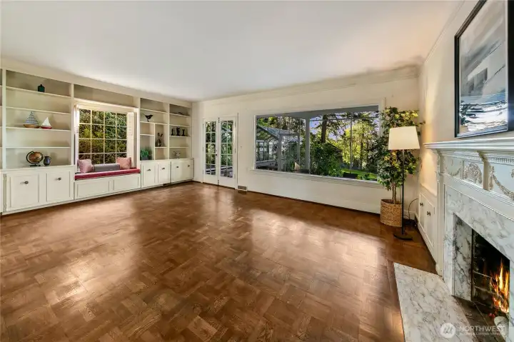 Bathed in natural light and graced with original hardwood parquet floors, this spacious main living area invites both quiet reflection and joyful gathering. A picture window anchors the room with a verdant forest view, while custom built-ins, a cozy window seat, and an elegant fireplace framed in marble lend warmth and character. The thoughtful craftsmanship reflects the home’s timeless charm, creating a place of comfort that feels rooted in its surroundings.
