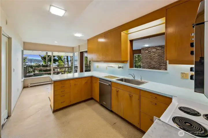 This light-filled kitchen is a preserved time capsule of midcentury design, with vintage cabinetry, cheerful aqua countertops, and generous workspace overlooking the lake. Picture windows flood the room with natural light and frame views of the gardens and water beyond, inviting moments of inspiration while cooking. Whether you choose to restore its retro charm or reimagine it entirely, the space offers an incredible canvas and connection to the surrounding beauty of Evergreen Point.