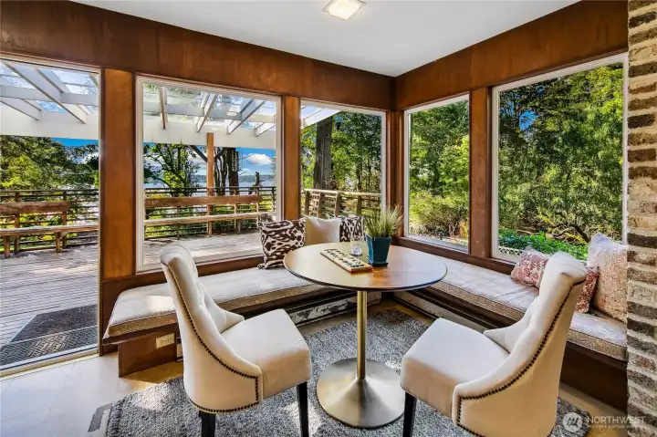 Wrapped in windows and warmth, this cozy corner nook offers a perfect perch to begin your day or unwind at dusk. Surrounded by lush woodland and filtered lake views, the built-in seating and natural wood paneling evoke a sense of timeless comfort. Just beyond, the adjacent patio and trellis-covered outdoor space blur the line between inside and out—offering a serene setting for slow mornings, afternoon tea, or gathering with friends amid the tranquility of the Evergreen Lakeshore Preserve.