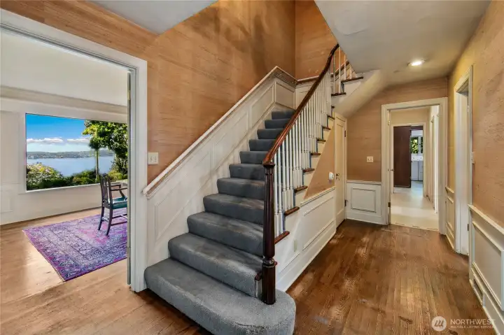 This gracious entry hall sets the tone for the home’s timeless character, with classic millwork, original hardwoods, and a sweeping staircase that hints at the history held within these walls. Natural light spills in from surrounding rooms, offering glimpses of lake views and garden greenery beyond. The layout invites both formal entertaining and everyday ease, connecting the heart of the home with its peaceful lakeside setting.