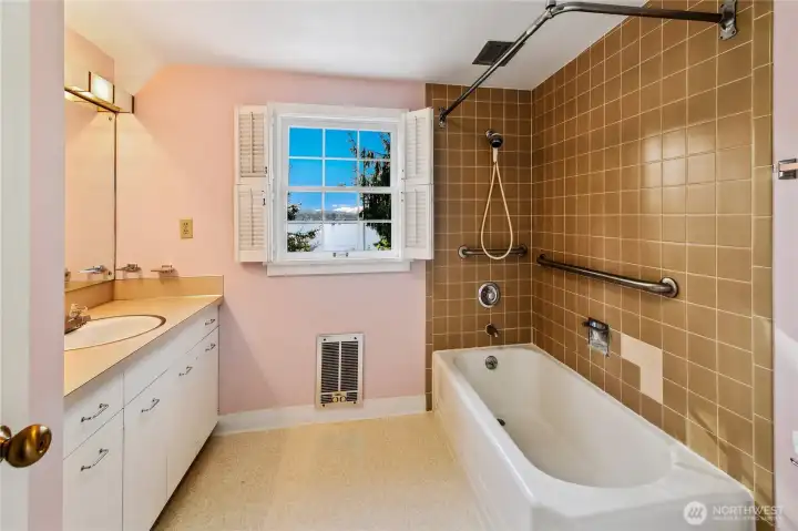This vintage bath retains charming mid-century details, from the warm ceramic tile to the classic built-in vanity with double sinks. A shuttered window offers natural light and a peek at Lake Washington beyond, inviting calm reflection. With both a soaking tub and shower, the space is primed for restoration or ready to serve as a nostalgic nod to the home's enduring character.