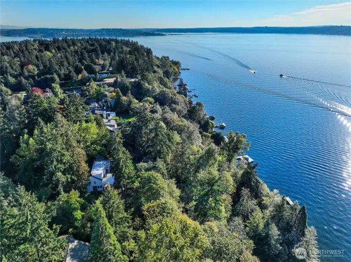 With boats skimming the calm surface of Lake Washington, this aerial view captures the expansive reach of the Evergreen Lakeshore Preserve and its surroundings. The shoreline stretches peacefully to the south, where forested slopes give way to deep blue waters, offering a sense of both seclusion and connection to the greater landscape. This is a place where privacy, nature, and possibility coexist.