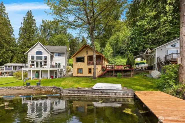 Front of home featuring spacious side deck, dock, and yard perfect for entertainment.