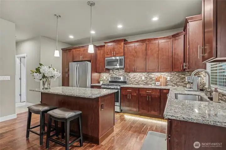 Kitchen view from dining, nice island with power, beautiful granite, full tile backsplash, and the custom cabinetry is simply stunning. Upper left leads to your garage and utility room.