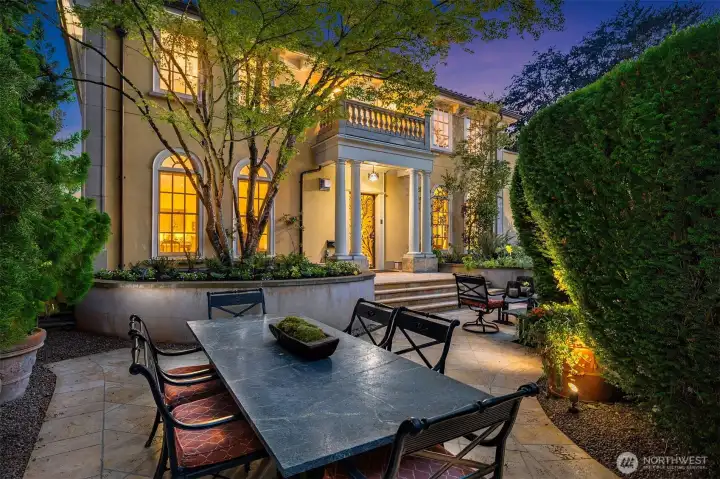 The lovely front courtyard features a large stone patio with dining and seating areas surrounded by thick privacy hedges.