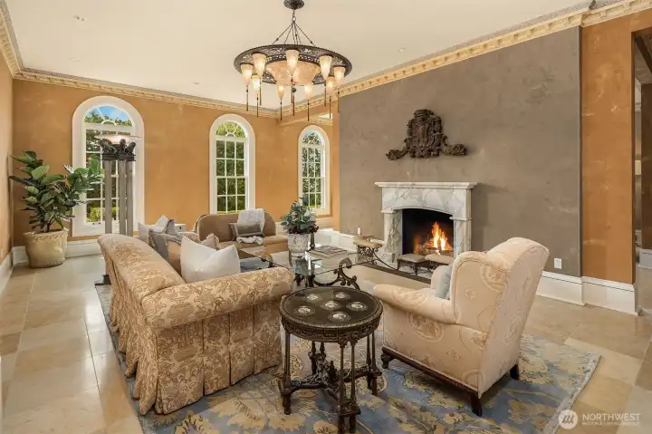 A grand entertaining living room with tall classic windows, beautiful silk Fortuny ceiling lamp, and custom fireplace designed by NW Terrazzo and Stone.