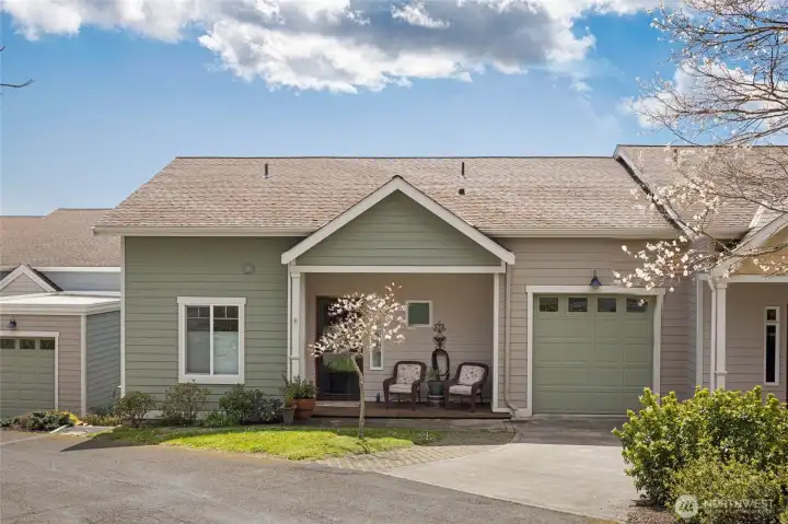 The charming single-level condominium presents exceptional curb appeal with its classic sage-green lap siding, covered front porch, and attached garage framed by a blossoming ornamental cherry tree. Thoughtfully maintained landscaping and a welcoming covered sitting area invite you to enjoy the mild Pacific Northwest climate year-round.