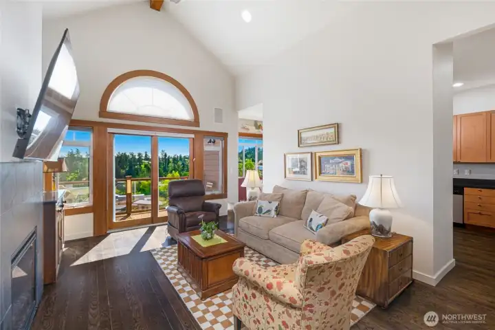 Dramatic vaulted living room with soaring cathedral ceilings, a signature arched window, and sliding door that frame breathtaking views of Friday Harbor, flooding the space with natural light and an airy, open feel.