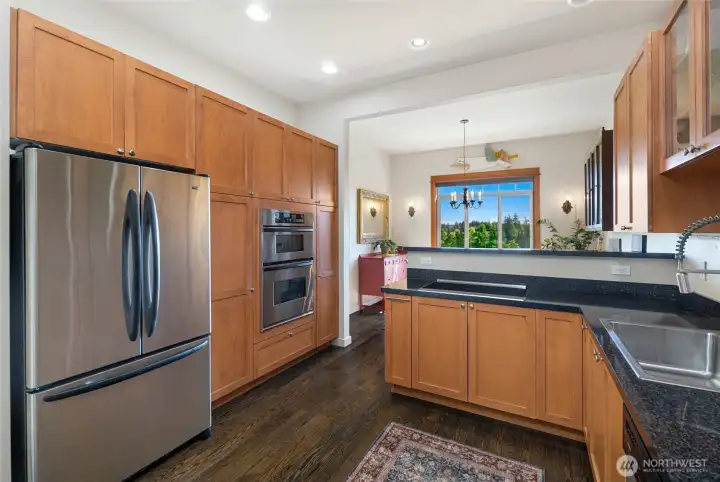 Generously sized kitchen boasts premium stainless steel appliances including a French-door refrigerator and double wall oven, custom wood cabinetry reaching to the ceiling, and rich hardwood floors throughout.