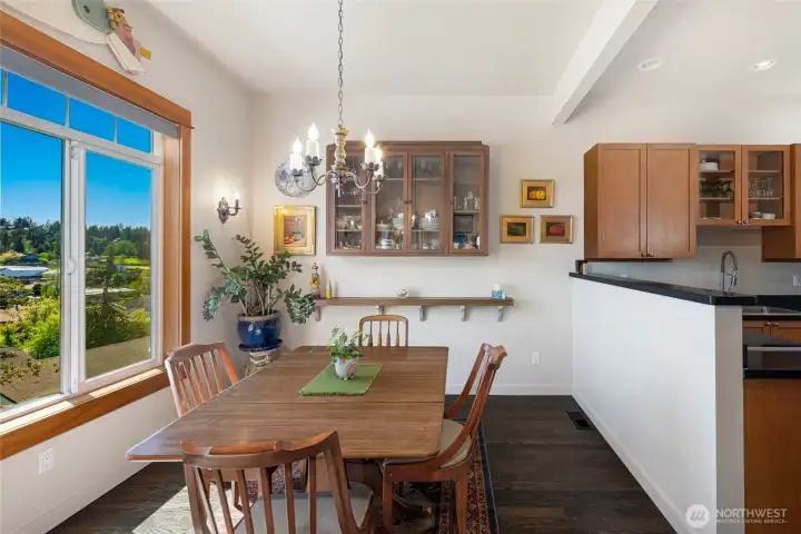 The sun-drenched dining room features warm wood tones, a classic chandelier, and a large picture window framing lush outdoor views, creating an inviting space for entertaining. Kitchen to the right