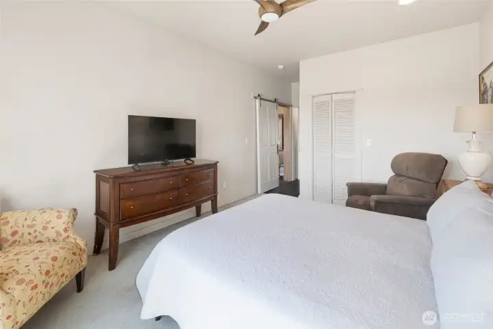 The serene primary bedroom offers plush carpeting, walk-in closet, a ceiling fan, and a sliding barn-style door alongside a 3/4 en-suite bath, creating a private and restful sanctuary. Generous space accommodates a king bed with room for comfortable seating and media.