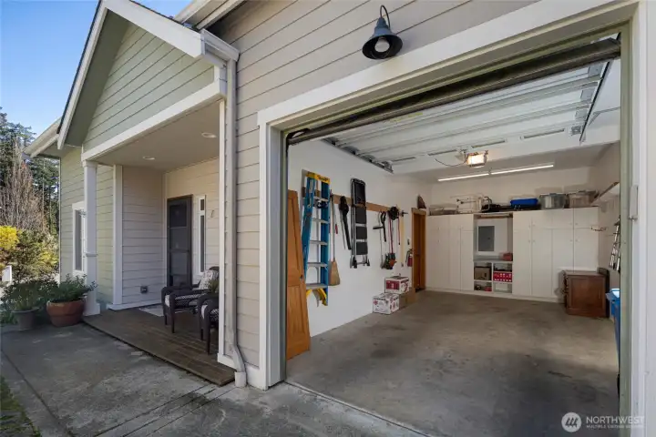 The attached garage presents a wide roll-up door with automatic opener, and a charming covered side entry, all set against the condo's crisp sage-green lap siding. Plenty of organized interior cabinetry and tool storage.