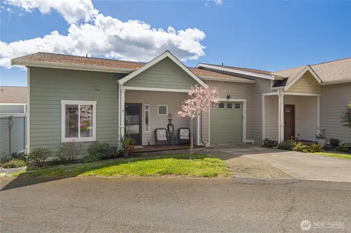 A picturesque street-facing elevation reveals the condo's craftsman character, accented by a blooming cherry tree and manicured grounds that burst with color each spring. The covered entry porch and clean architectural lines reflect the quality construction and meticulous upkeep throughout this desirable community.