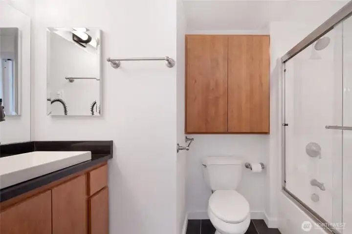 The lower level studio's well-appointed full bathroom features a sleek dark-countertop vanity, warm wood cabinetry, and a full tub-shower combination with sliding glass doors.
