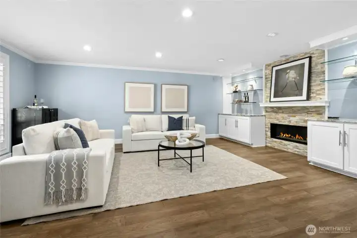 Custom lighting, built-in storage, display shelving, and a sleek gas fireplace set against a stacked stone backdrop bring warmth and character to the space.  East-facing windows welcome the morning light, while plantation shutters allow the ambiance to shift effortlessly from bright and airy to cozy on colder nights.