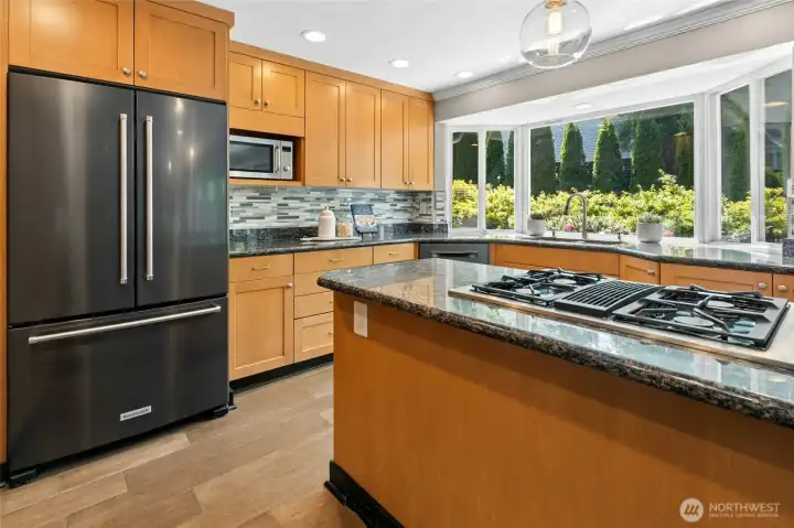 Thoughtfully designed for both function and flow, the kitchen offers abundant cabinetry, slab granite counters, stainless appliances, and a gas cooktop with a downdraft vent to use while cooking.