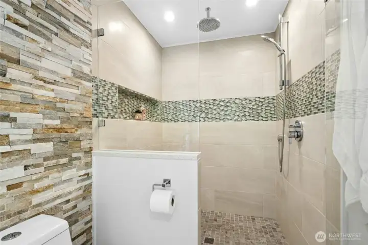 The walk-in shower features sleek glass surrounds, floor-to-ceiling tile, and a ceiling-mounted rainfall shower head for a true retreat-like feel.