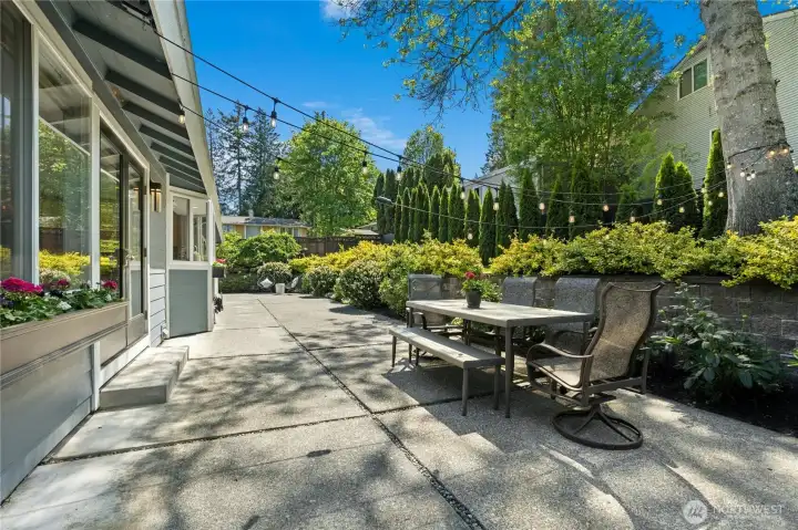 Designed for effortless outdoor living, the expansive patio offers multiple spaces to gather, dine, and unwind beneath café lighting and mature trees.