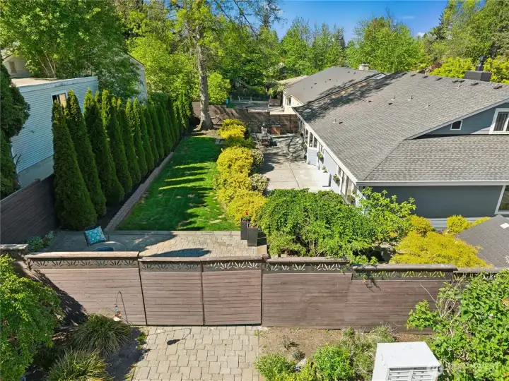 From above, the thoughtfully terraced backyard reveals multiple outdoor living spaces woven together by mature landscaping, privacy fencing, and expansive patios.  The design balances beauty and function with a handy service access gate, an upper-level firepit retreat, and distinct spaces for gathering, relaxing, play, and quiet retreat.