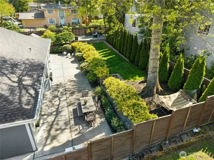 The terraced backyard unfolds into a series of inviting outdoor spaces, including an expansive patio, shaded hammock retreat, upper-level firepit area, and broad lawn framed by mature landscaping.