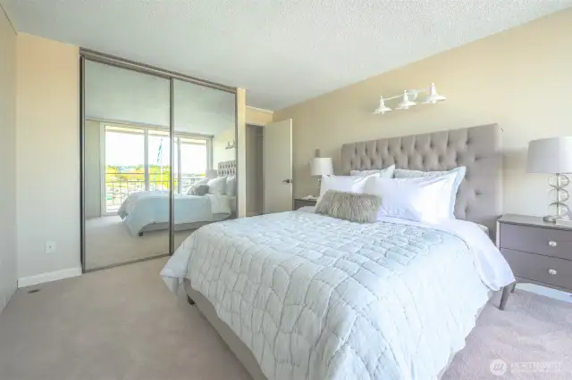 Sunlight filters through mirrored doors in this spacious primary suite—offering generous storage, tranquil tones, and effortless comfort to start and end your day.