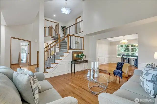 The formal living room showcases the home's elegance with a stunning view of the grand staircase and a beautiful chandelier. Natural light highlights the spacious layout and timeless design elements.