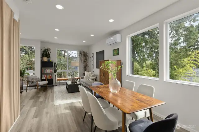 An open dining space that flows effortlessly into the living area, filled with light from large windows that offer views of the surrounding greenery.