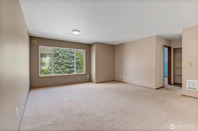 Spacious and bright living room with a large picture window overlooking lush evergreens—your perfect spot to unwind.