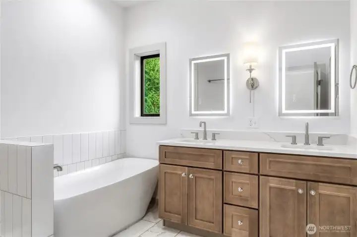 Primary bath featuring a freestanding soaking tub, double vanity and illuminated mirrors. Primary bath featuring a freestanding soaking tub, double vanity and illuminated mirrors.