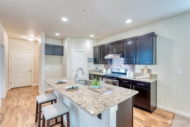 Past the living room and dining space is the gourmet kitchen adorned with warm hardwood flooring, granite countertops, rich maple cabinetry with crown molding, gas cooking, a center island with bar seating and pantry.