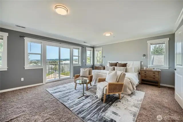 Wake up to breathtaking views in this serene primary suite, where natural light floods in through a wall of expansive windows and sliding glass doors that open to a private balcony. The generous layout offers space for a cozy sitting area—ideal for morning coffee or evening relaxation. Soft gray walls, crisp white trim, and plush carpeting create a soothing palette, while recessed lighting and dual night sconces enhance both function and ambiance. Thoughtfully designed for comfort and style, this retreat offers the perfect blend of peace, privacy, and panoramic beauty.