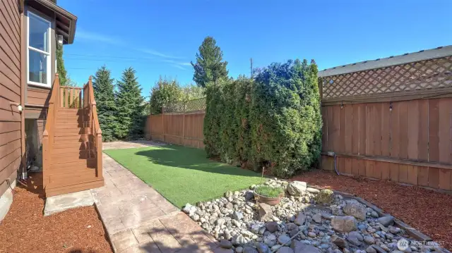 Enjoy low-maintenance living in this private, fully fenced backyard retreat. Featuring lush turf grass, a stamped concrete walkway, and mature landscaping, this space is ideal for entertaining or relaxing outdoors. A charming rock garden adds visual interest, while the tall evergreens and lattice-topped fencing provide added privacy. Whether you're hosting guests or unwinding with a book, this thoughtfully designed outdoor area offers the perfect blend of beauty and function.