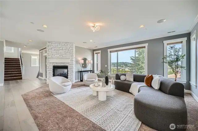 Step into modern elegance with this stunning living room that perfectly blends comfort and sophistication. Flooded with natural light from expansive windows, the space offers breathtaking views and a serene atmosphere. The focal point is a striking white stacked-stone fireplace, adding warmth and architectural interest. Rich gray accent walls complement the neutral-toned carpeting and wide-plank hardwood floors, creating a stylish contrast. The layout is both inviting and functional, featuring a designer-curved sectional, cozy swivel chairs, and a textured area rug that anchors the room. Ideal for both everyday living and entertaining, this space is a true showpiece.