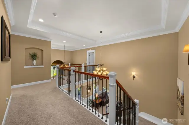 Landing shows continued double crown molding, wrought iron railing, art niche, open ceilings to lower level.
