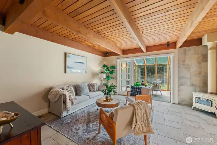 Inviting living room with beautiful wood ceilings that echo the natural surroundings, creating a warm, grounded feel and opening to the sunroom beyond.