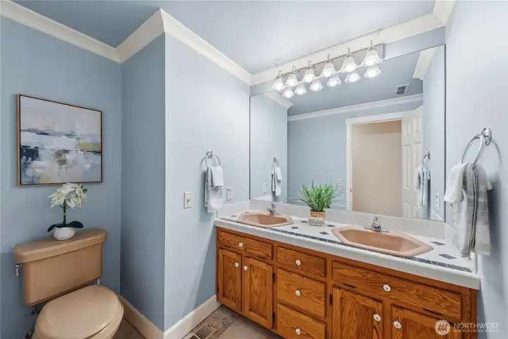 Bright main level bathroom featuring beautiful crown molding that adds a polished, finished touch to the space, along with dual sinks and warm wood cabinetry.