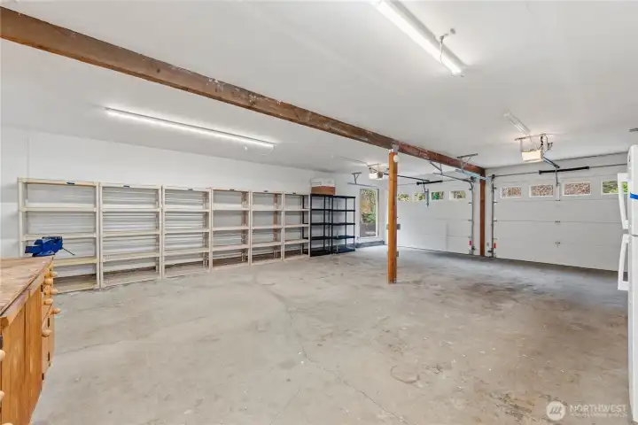 Oversized attached garage with two car doors offering ample space for vehicles, storage, or a workshop setup. The generous depth allows for flexible tandem-style parking, along with existing shelving for easy organization and storage.