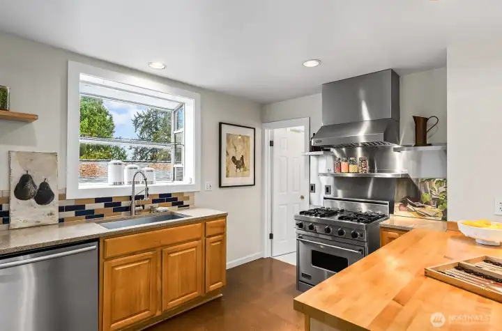 Quartz counters, tile backsplash, stainless steel appliances, wood cabinets, and a garden window above the sink.