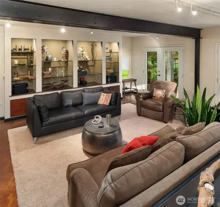 A comfortable lower-level gathering space features custom display shelving, abundant natural light, and French doors opening directly to a private garden patio.