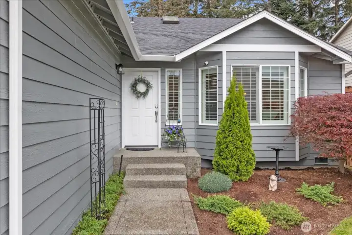 Inviting front entry framed by established landscaping, plantation shutters, & a warm welcoming feel.